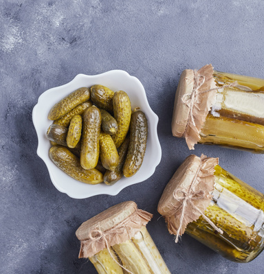 KI generiert: Ein Teller saurer Gurken neben eingelegten Gurkengläsern auf dunklem Untergrund.