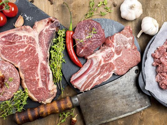 KI generiert: Verschiedene rohe Fleischsorten auf Schneidebrettern mit Kräutern, Chili und Knoblauch arrangiert.