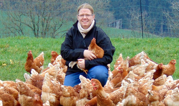 KI generiert: Eine Person kniet inmitten einer großen Gruppe brauner Hühner auf einer Wiese.