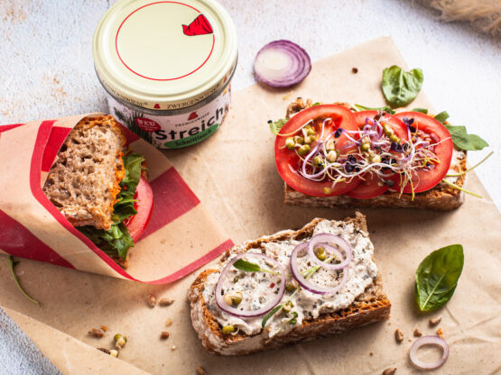 KI generiert: Vollkornbrote mit Aufstrich, Tomaten und Sprossen, daneben ein Becher "Streich's drauf" Schmelzcreme.