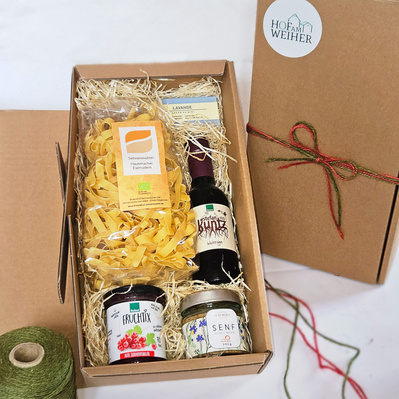 KI generiert: Geschenkbox mit Bio-Produkten: Nudeln, Fruchtaufstrich, Senf, Essig. Text: "HOF am WEIHER".